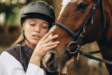 Fototapeta premium A young female equestrian stands near her horse and prepares for a competition.