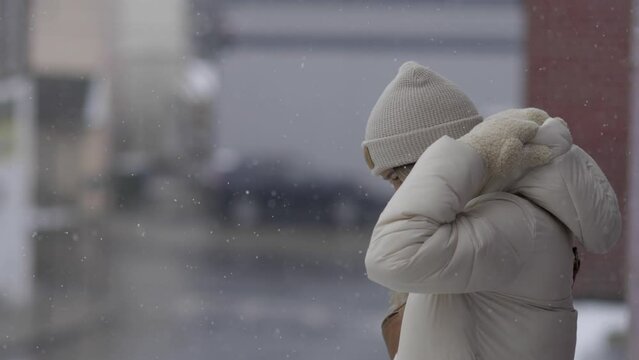 A woman pulls up her hood to protect herself from the falling snow
