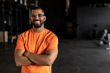 Portrait of bearded biracial young man with arms crossed smiling and standing in gym