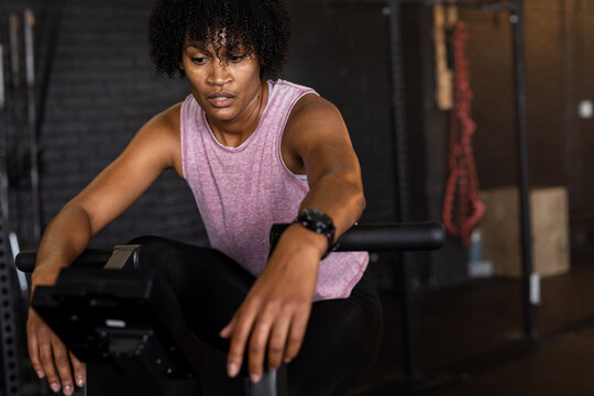 Biracial exhausted young woman with afro hair cycling on exercise bike in gym