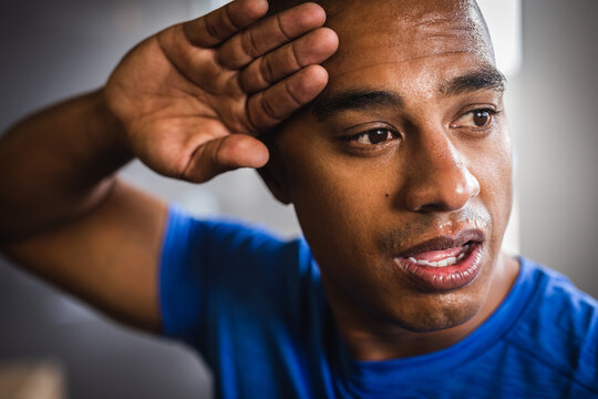 Closeup of tired biracial young man wiping sweat from forehead while exercising in gym