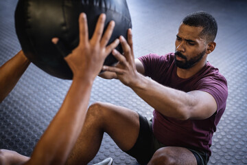 High angle view of biracial young male friends exercising with fitness ball while sitting in gym