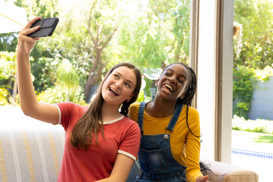 Happy diverse teenager girls friends sitting on sofa and taking a selfie