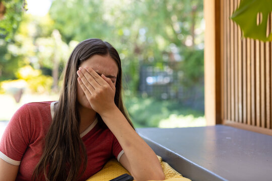 Sad caucasian teenager girl sitting on sofa, covering her face and crying