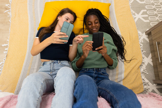 Happy diverse teenager girls friends laying on floor and using smartphones