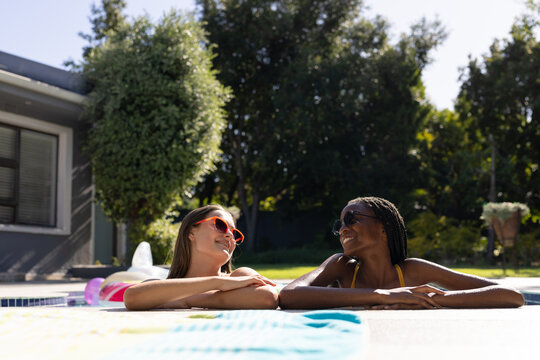 Portrait of happy diverse teenager girls friends looking at each other and smiling in swimming pool