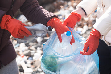 close up woman hands wearing gloves collecting plastic garbage to help clean up beach and public...