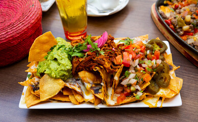 Plate of traditional Mexican nachos with meat, vegetables and sauces