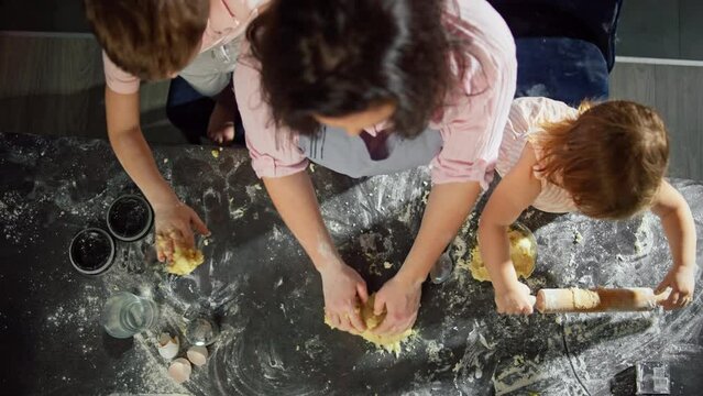 Mother, son and daughter knead the dough together. The family is preparing pastries at home in the kitchen. The lifestyle of happy children and parents spending time together.