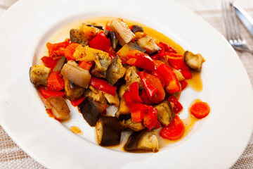 Plate of appetizing ragout of baked chopped aubergine, carrot, tomato, bell pepper and pork bacon slices for dinner..