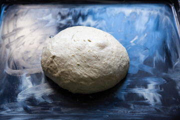 a ball of dough on baking tray smeared with butter. homemade wood fired pizza