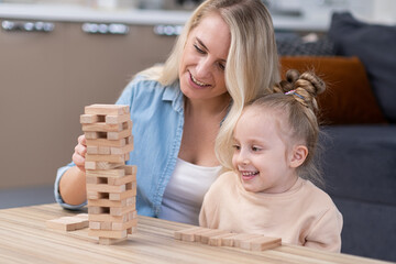 wooden tower blocks game on the table. Mom and girl child enjoyinh playing together. Happy family playing board games at home.