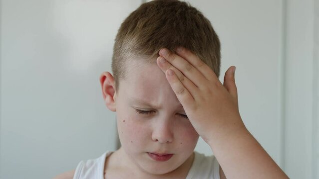 Portrait of european white boy scratching forehead with hand, close-up. Child rubs irritated, itchy skin, shrugs shoulders in confusion, blinks eyes. Acute allergic reaction of body to food and air.