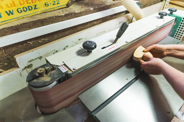 Unrecognizable carpenter working on a wooden piece using professional grinding machine. Wood goods creation process. High quality photo