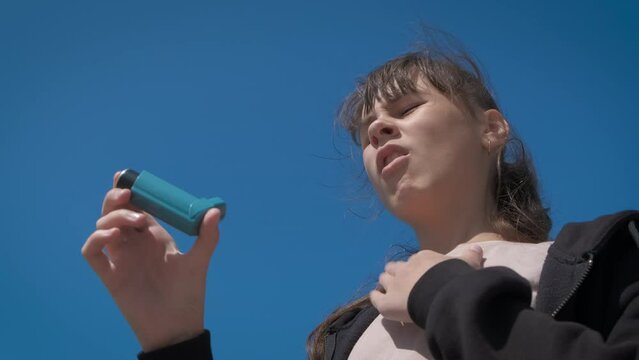 Sunny day with girl with asthma. A view of stressed teen use an inhaler during hard breathing under the hot sunny rays in summer.
