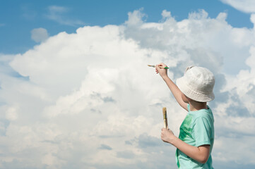 Young artist paints a beautiful sky and three-dimensional clouds with brushes in his hands
