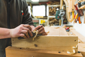 Male carpenter working with plane on wooden plank. Woodworking workshop interior in the background. High quality photo