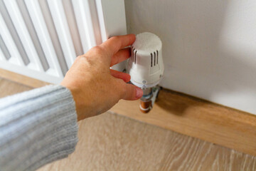 Human's hand adjusting radiator temperature. Energy crisis and cost of living crisis concept