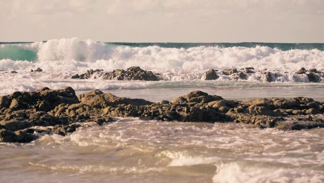 Sea waves crash against the coastal rocks on the sandy beach.
