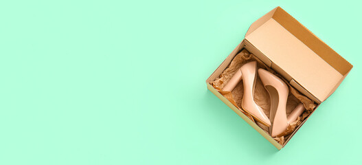 Cardboard box with high heeled shoes on turquoise background with space for text