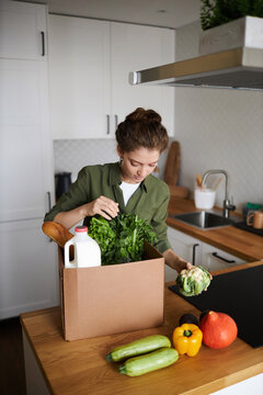 Vertical Portrait Of Young Woman Unpacking Fresh Grocery Delivery In Kitchen