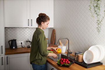 Minimal side view portrait of young woman washing vegetables in kitchen, copy space
