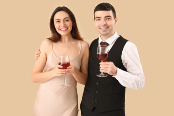 Elegant young couple with glasses of wine on beige background