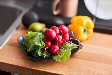 Closeup of fresh organic radishes in little plastic plate on kitchen counter, copy space