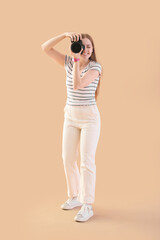 Young female photographer with professional camera on beige background