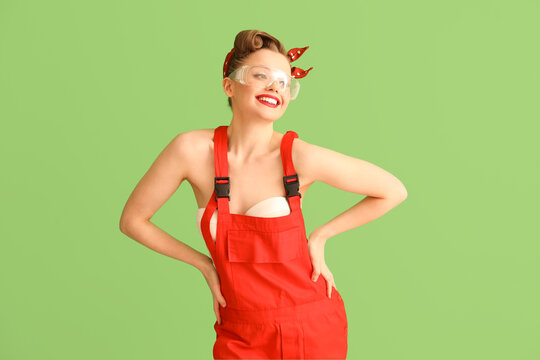 Young pin-up woman in safety goggles and uniform on green background