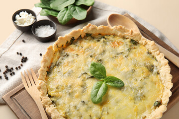 Board with delicious quiche and spinach leaves on beige background