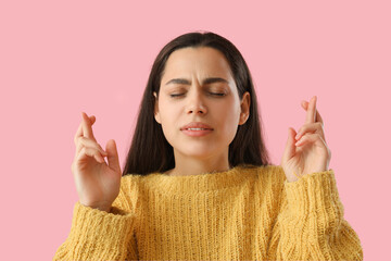 Beautiful young woman crossing fingers on pink background, closeup