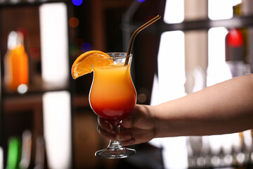 Woman holding glass of tasty Tequila Sunrise in bar