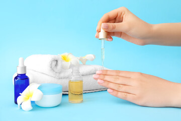 Woman applying oil onto cuticles on color background