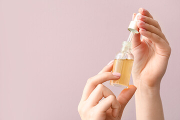 Female hands with bottle of cuticle oil against color background, closeup