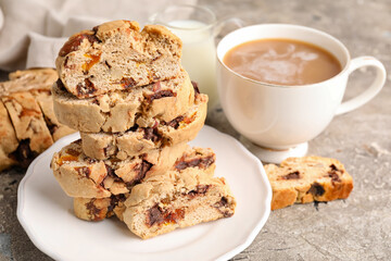 Plate with stack of tasty biscotti cookies and cup of coffee on grunge background, closeup