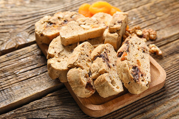 Board with delicious biscotti cookies and dried apricots on wooden background