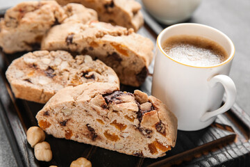 Board with delicious biscotti cookies and cup of coffee on grey grunge background