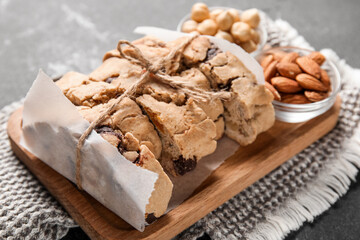 Board with delicious biscotti cookies and bowls of nuts on grey grunge background