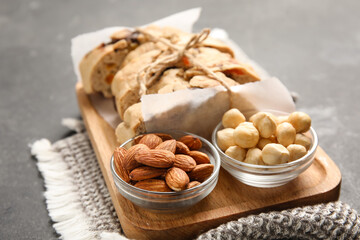 Board with delicious biscotti cookies and bowls of nuts on grey grunge background