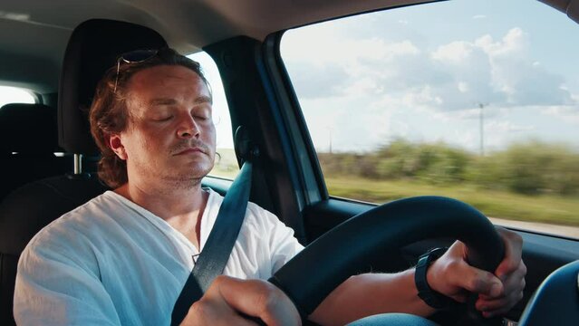 Tired sleepy young man drives the car on a highway and slowly closes his eyes. Man closes his eyes while driving a car and loses concentration