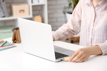 Woman using USB flash drive with modern laptop at table in office