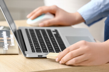 Fototapeta premium Woman with USB flash drive and laptop at wooden table, closeup