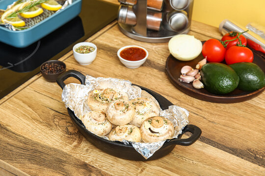 Baking dish with raw mushrooms, spices and vegetables on wooden table in kitchen