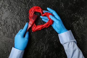 Woman in rubber gloves painting decorative heart with brush on dark background
