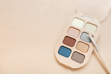 Palette of eyeshadows with brush on beige background, closeup