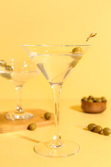 Glasses of martini with olives on yellow background
