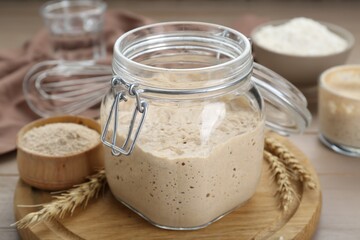 Leaven and ears of wheat on beige wooden table