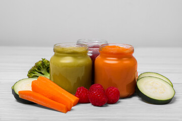 Jars with healthy baby food and ingredients on white wooden table