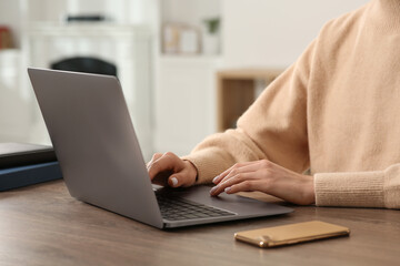 Woman working with laptop at wooden desk indoors, closeup